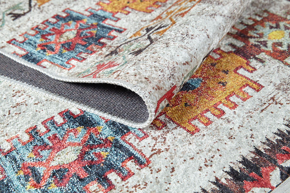 A close-up of the Ethno Expanse - Machine-Washable Rug (JR5046) displays vibrant geometric patterns in red, blue, orange, and yellow. The durable rug is partially folded, revealing its textured gray underside—perfect for high-traffic spaces.