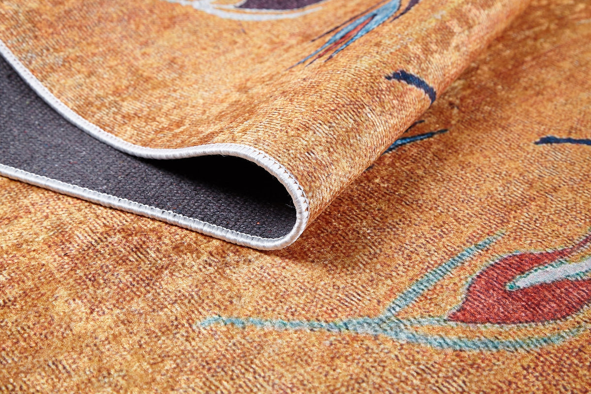 A close-up of the Floral Mosaic - Washable Rug - JR1720 highlights its orange and brown pattern, textured fabric, stitched edge, and a folded corner showing the dark non-slip backing—perfect for high-traffic areas.