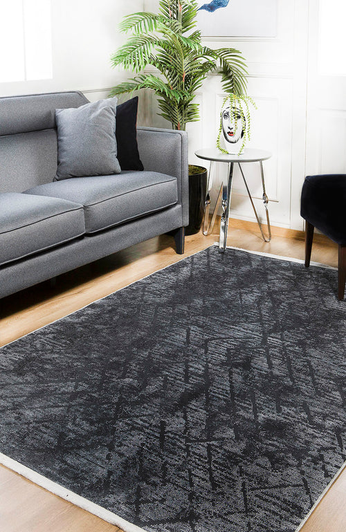 Load image 1 in gallery view. A modern living room features a gray sofa, black chair, and the Geometric Gems - Washable Rug - JR1342, ideal for high-traffic wooden floors. A round side table displays a face planter with leafy greens next to a lush green potted plant.