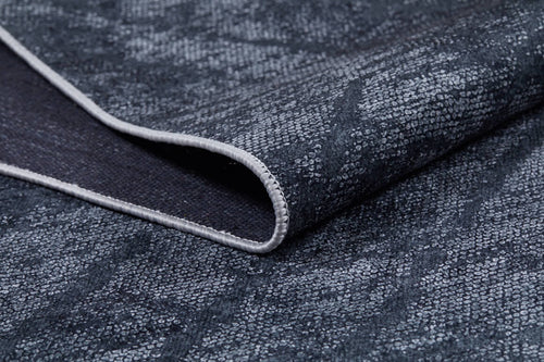 Load image 1 in gallery view. A close-up of the Geometric Gems - Washable Rug - JR1342 reveals its folded, textured dark gray fabric with a subtle pattern and light stitching—ideal for high-traffic areas due to its washable design.