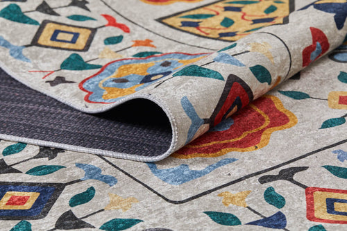 Load image 1 in gallery view. A close-up of the Global Gathering - Washable Rug - JR608 shows its multicolor floral and geometric design in red, blue, yellow, green, and black on a light background, with the corner lifted to reveal its textured underside.