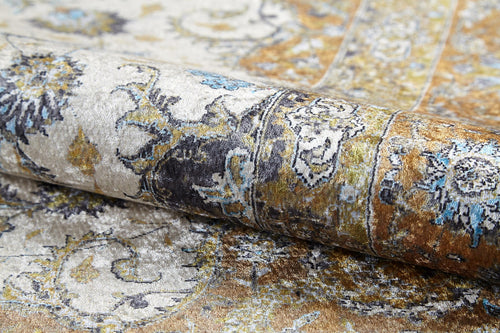 Load image 1 in gallery view. Close-up of the Golden Oasis - Washable Rug (JR1930), rolled up to reveal intricate floral and paisley patterns in gold, blue, black, and cream—durable, washable, and ideal for high-traffic areas with its textured, vintage look.