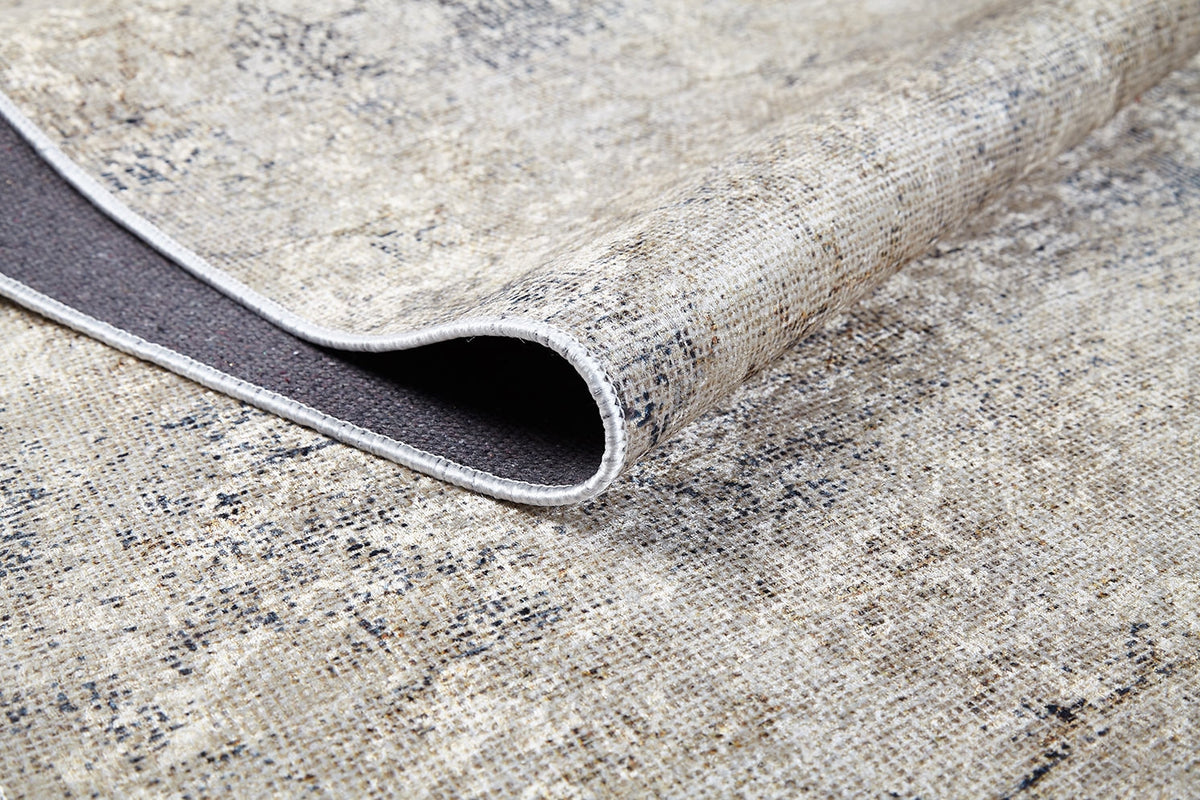A close-up of the Graceful Tapestry - Washable Rug - JR1975 shows a cream and beige flat weave with one corner folded, revealing its dark underside and textured fabric. This washable rug boasts elegant patterns and practical design.