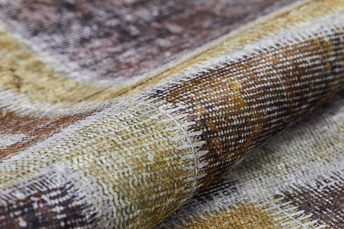 A close-up of Gridiron Glow - Washable Rug - JR183 reveals detailed stitching on its textured, woven fabric in earthy tones like brown, beige, and olive green—ideal for high-traffic areas with a slightly raised fold.