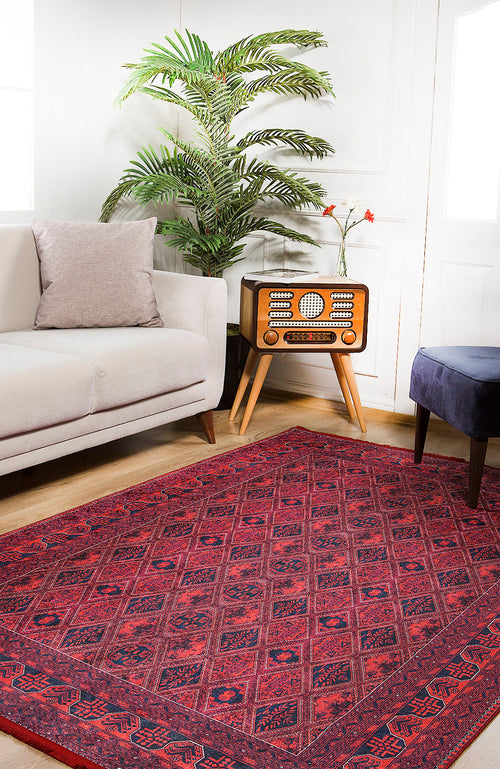 Load image 1 in gallery view. A cozy living room features the Imperial Impressions - Washable Rug - JR1132, ideal for high-traffic areas, a white sofa with a gray pillow, vintage radio on a wooden stand, potted plant, dark blue ottoman, and bright natural light.
