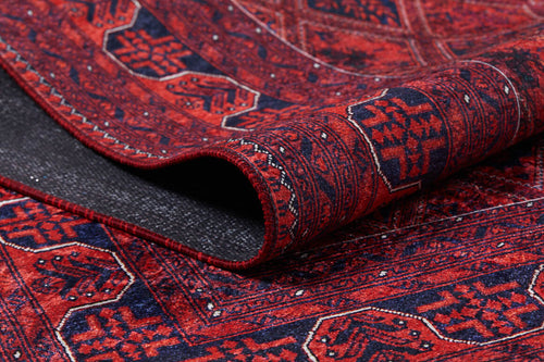 Load image 1 in gallery view. A close-up of the Imperial Impressions - Washable Rug - JR1132 shows its red and navy geometric pattern. The curled edge reveals the dark underside and texture, making this rug ideal for high-traffic areas.