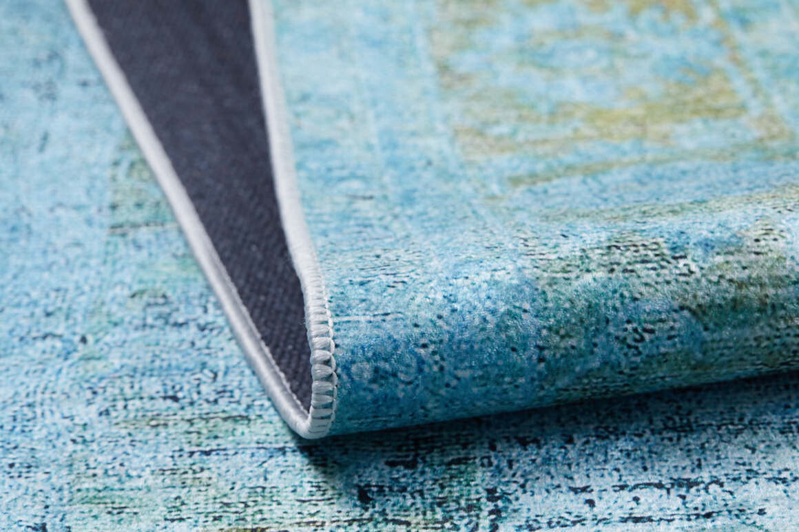 A close-up of the Imperial Jewel - Washable Rug - JR162 in blue and green, ideal for high-traffic areas, shows one corner folded to reveal its dark non-slip backing and white stitched edge.