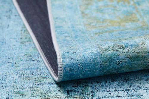 Load image 1 in gallery view. A close-up of the Imperial Jewel - Washable Rug - JR162 in blue and green, ideal for high-traffic areas, shows one corner folded to reveal its dark non-slip backing and white stitched edge.