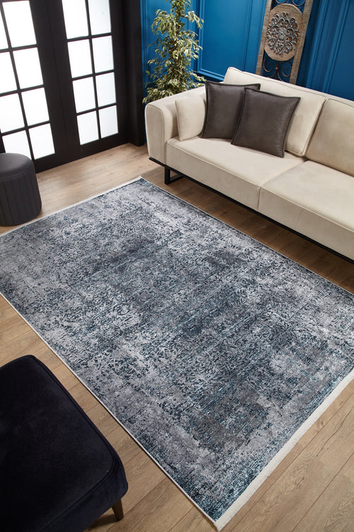 Load image 1 in gallery view. A modern living room with a beige sofa, dark accent pillows, the Imperial Lace Washable Rug (JR1607) in blue on wooden floors—ideal for busy spaces—a black ottoman, green plant, and blue paneled walls with decorative art.