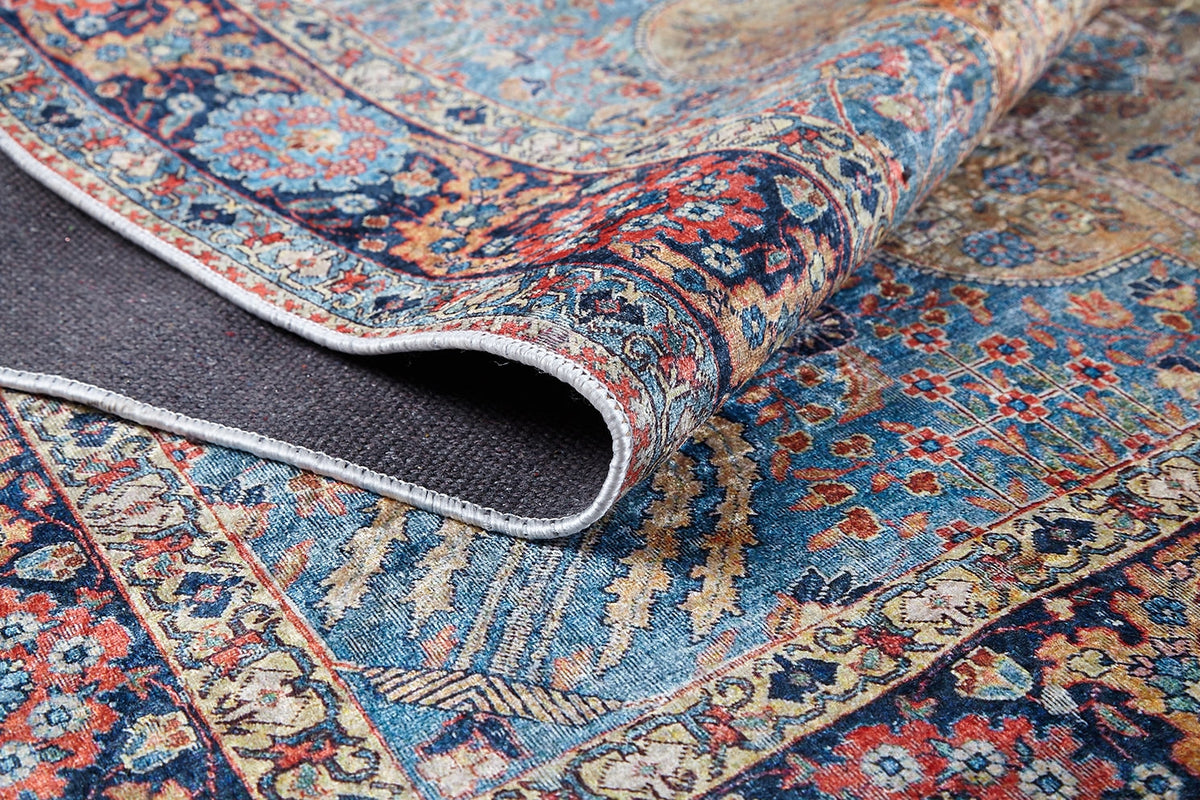 A close-up of the Imperial Weave - Washable Rug - JR1969 shows its colorful Persian blue pattern with red, yellow, and beige designs. The turned-up corner reveals texture and weave—perfect for high-traffic areas and easy to maintain.