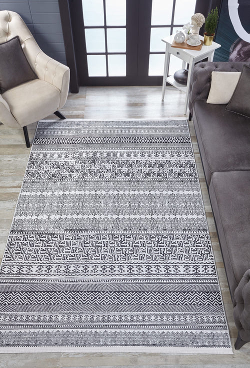 Load image 1 in gallery view. A living room featuring the Indie Impressions - Washable Rug - JR1648 in gray-anthracite, a beige armchair, gray sofa, small white side table with plants, and large black-framed windows—ideal for high-traffic areas.