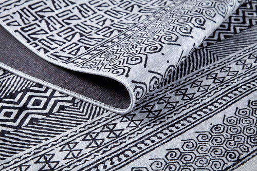 Load image 1 in gallery view. A close-up of the Indie Impressions - Washable Rug - JR1648 showcases its black and white geometric and swirl patterns, with the corner of the monochrome rug slightly folded to display its washable design.
