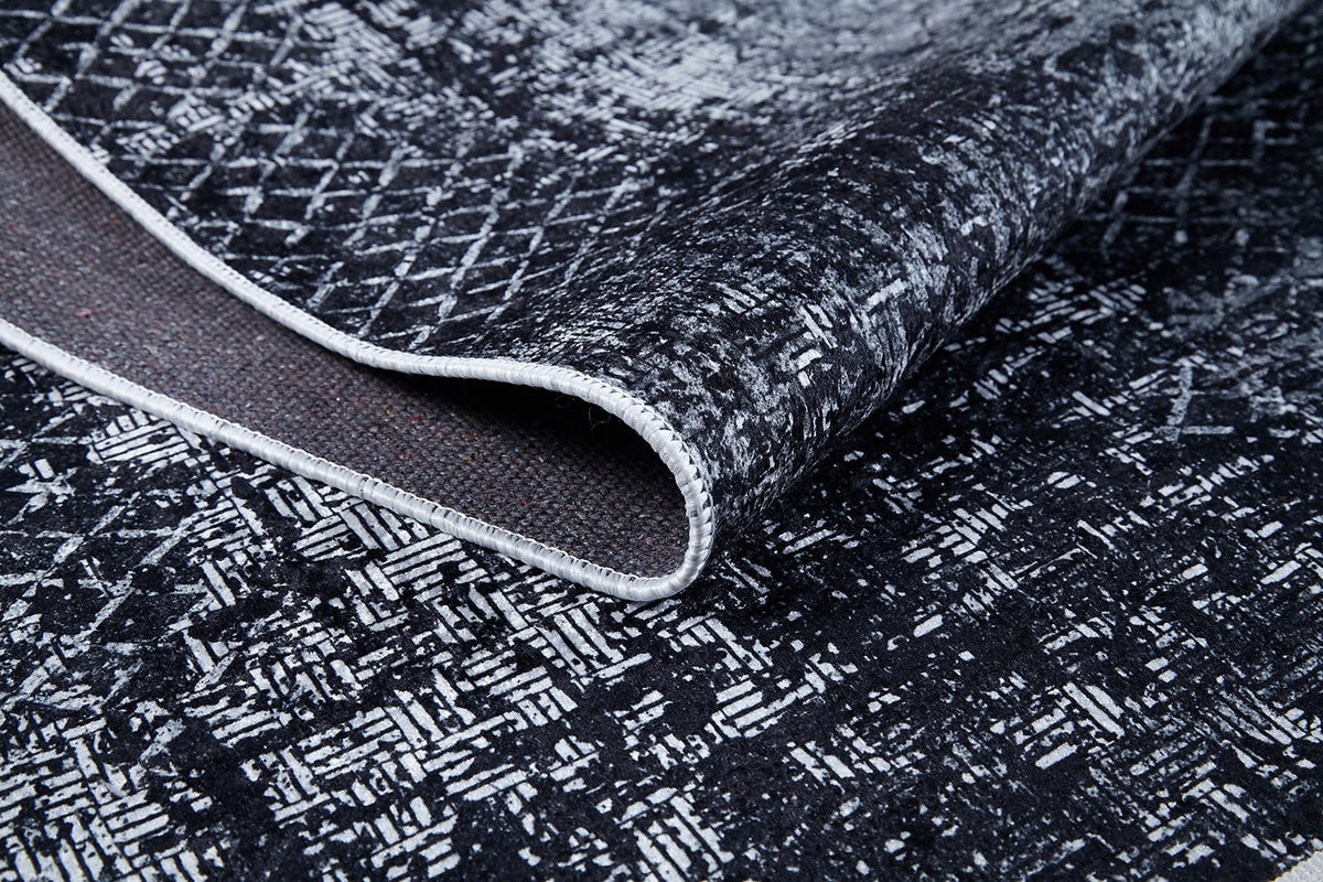 A close-up of the Infinity Garden - Washable Rug - JR1749 shows its black and white abstract geometric pattern, textured surface, lifted edge to reveal the underside and border stitching—durable and ideal for high-traffic areas.