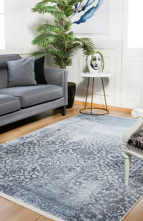 Load image 1 in gallery view. A modern living room features a gray sofa, a white accent chair, the Intricate Scroll - Washable Rug - JR342 for high-traffic areas, a small round side table with a decorative vase, a tall green plant, and framed wall art.