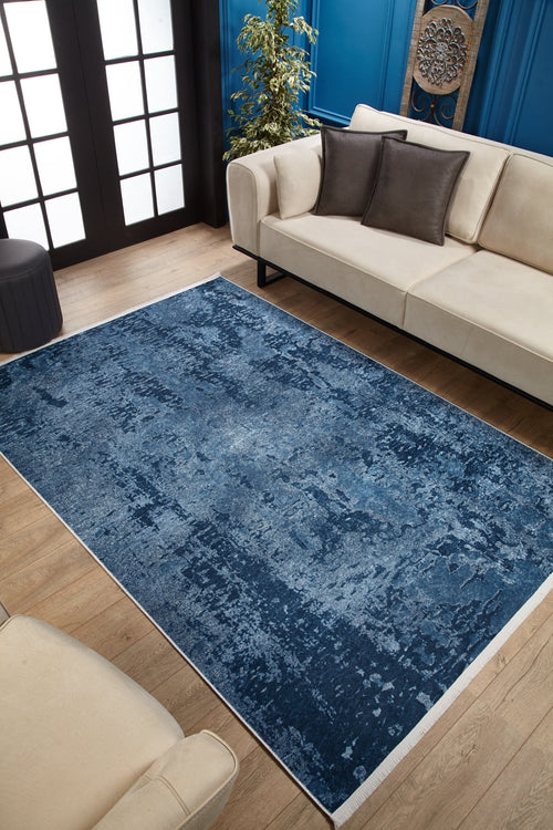 Load image 1 in gallery view. A modern living room features the Ivory Whisper - Washable Rug - JR1628, ideal for high-traffic areas, set on a wooden floor with beige sofas, dark accent pillows, a potted plant, and blue walls with decorative molding and art.