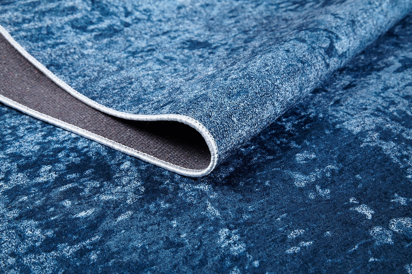 A close-up of the Ivory Whisper - Washable Rug - JR1628 with a corner flipped over, showing its gray woven underside and white stitching—perfect as a washable rug for high-traffic areas.