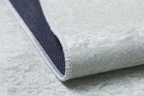 Load image 1 in gallery view. A close-up of the Joyful Elephant - Machine-Washable Rug JRC026 in light gray, featuring a soft, velvety texture. One corner is lifted to reveal its dark backing and white stitched edge.