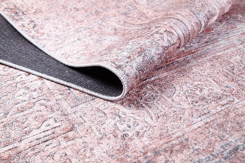 Load image 1 in gallery view. A close-up of the Luxurious Design - Washable Rug - JR1924 in soft pink, with a folded corner showing its textured black underside and faded beige and brown patterns—ideal for adding style to busy spaces.