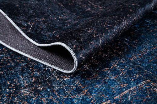 Load image 1 in gallery view. A close-up of the Luxurious Fleur - Washable Rug - JR1897 in dark blue and black with subtle brown patterns, showing a folded corner to reveal the underside and edge stitching—perfect for high-traffic spaces.
