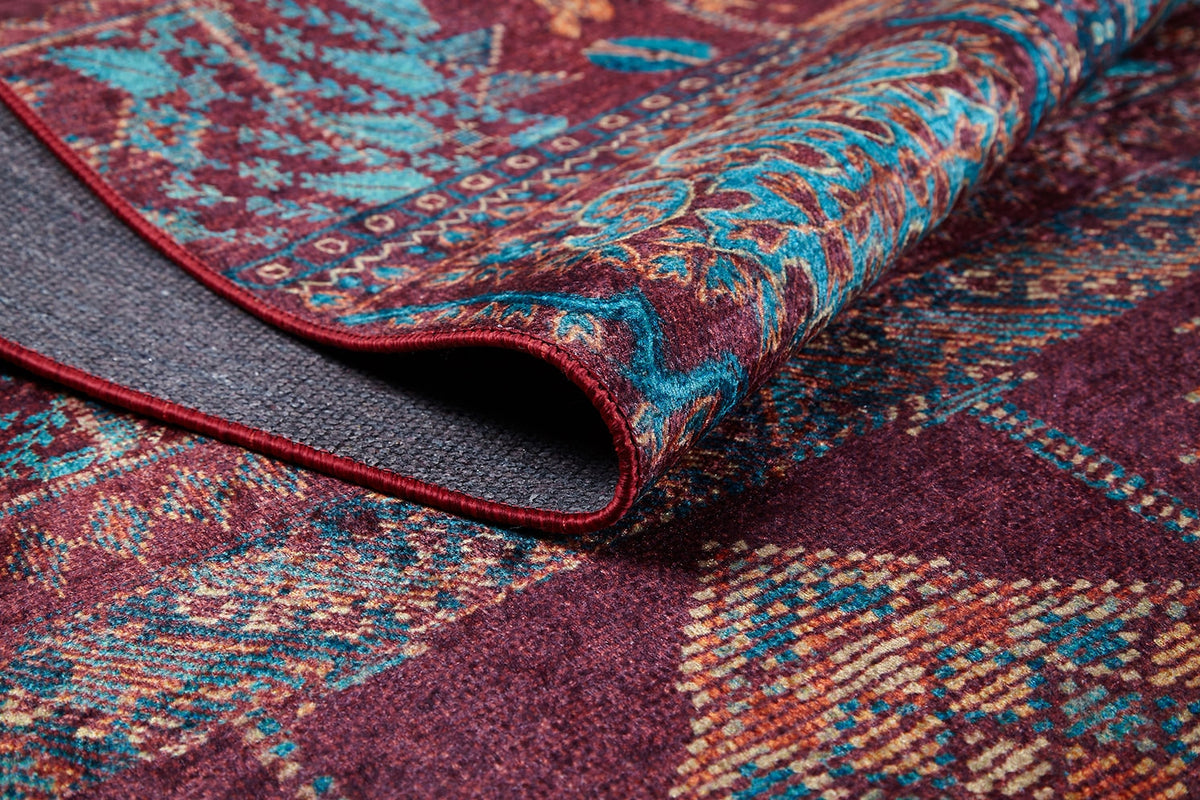 A close-up of the Majestic Mandarin - Washable Rug - JR1863, featuring folded, intricate geometric and floral designs in blue, yellow, and teal on a maroon background—its visible texture makes it ideal for high-traffic areas or stylish décor.