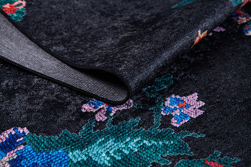 Load image 1 in gallery view. A close-up of the Meadow Dream - Washable Rug - JR2001 in black shows its lifted corner and underside. Its colorful floral pattern in green, blue, purple, and pink makes it ideal for high-traffic areas.