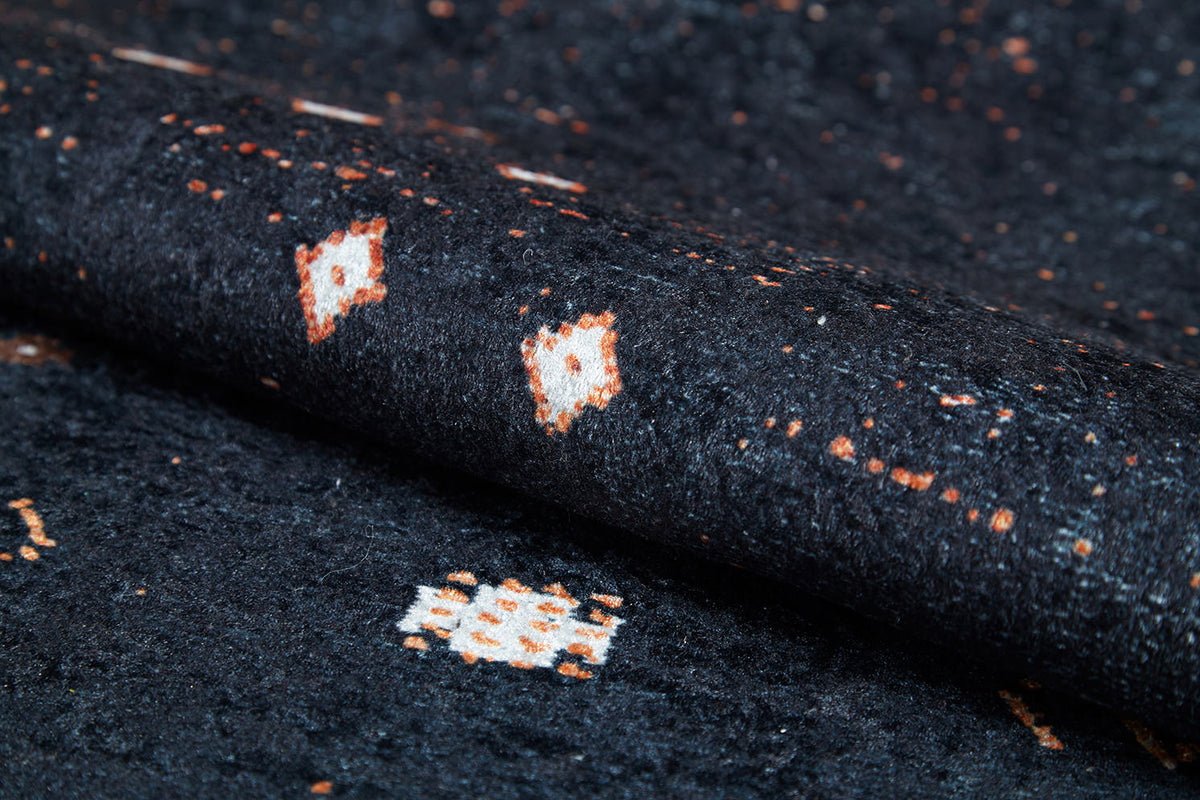 Close-up of the Midnight Majesty - Machine-Washable Rug (JRS5052), showing its dark textured surface with white and orange geometric patterns; durable for high-traffic areas and easy to clean.