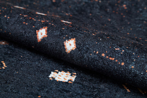 Load image 1 in gallery view. Close-up of the Midnight Majesty - Machine-Washable Rug (JRS5052), showing its dark textured surface with white and orange geometric patterns; durable for high-traffic areas and easy to clean.