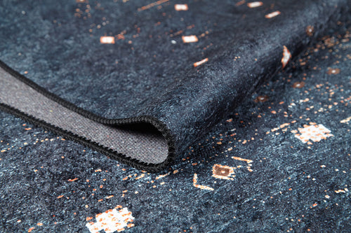 Load image 1 in gallery view. A close-up of the Midnight Majesty - Machine-Washable Rug (JRS5052) in blue, featuring textured fabric with small geometric white and orange patterns and a folded edge revealing the backing—ideal for high-traffic areas.