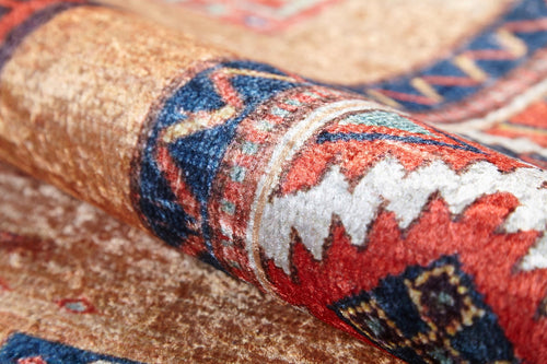 Load image 1 in gallery view. A close-up of the Navajo Nights - Washable Rug (JR1758) shows detailed geometric patterns in red, blue, white, and beige. Its textured surface and curved fold offer vibrant style that’s perfect for high-traffic areas.