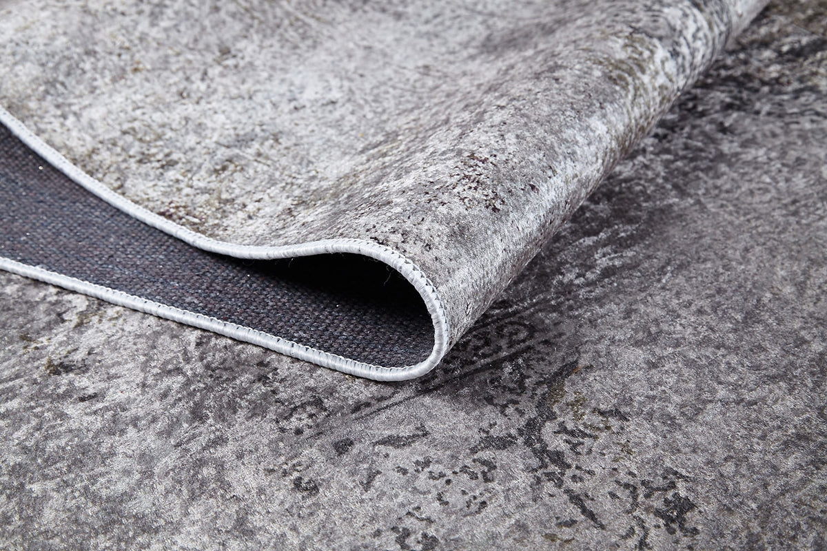 A close-up of the Noble Insignia - Washable Rug - JR1830 shows its gray textured surface with one corner lifted to reveal the black underside, highlighting durable material and stitching—perfect for high-traffic spaces.