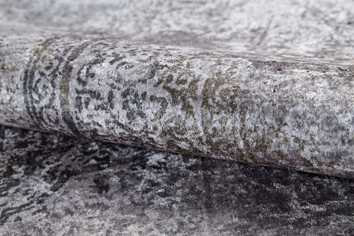 A close-up of the Noble Insignia - Washable Rug - JR1830 rolled up, showcasing its soft texture, grey tones, and subtle faded pattern. Its slightly distressed design makes it perfect for high-traffic areas.