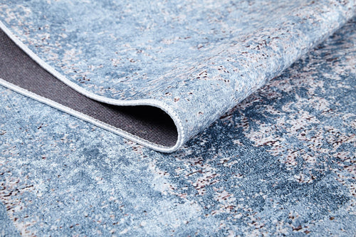 Load image 1 in gallery view. A close-up of the Old World Charm - Washable Rug - JR1606 shows its blue mottled, abstract pattern with a folded corner revealing the gray underside. This rug is both stylish and practical, perfect for high-traffic areas.