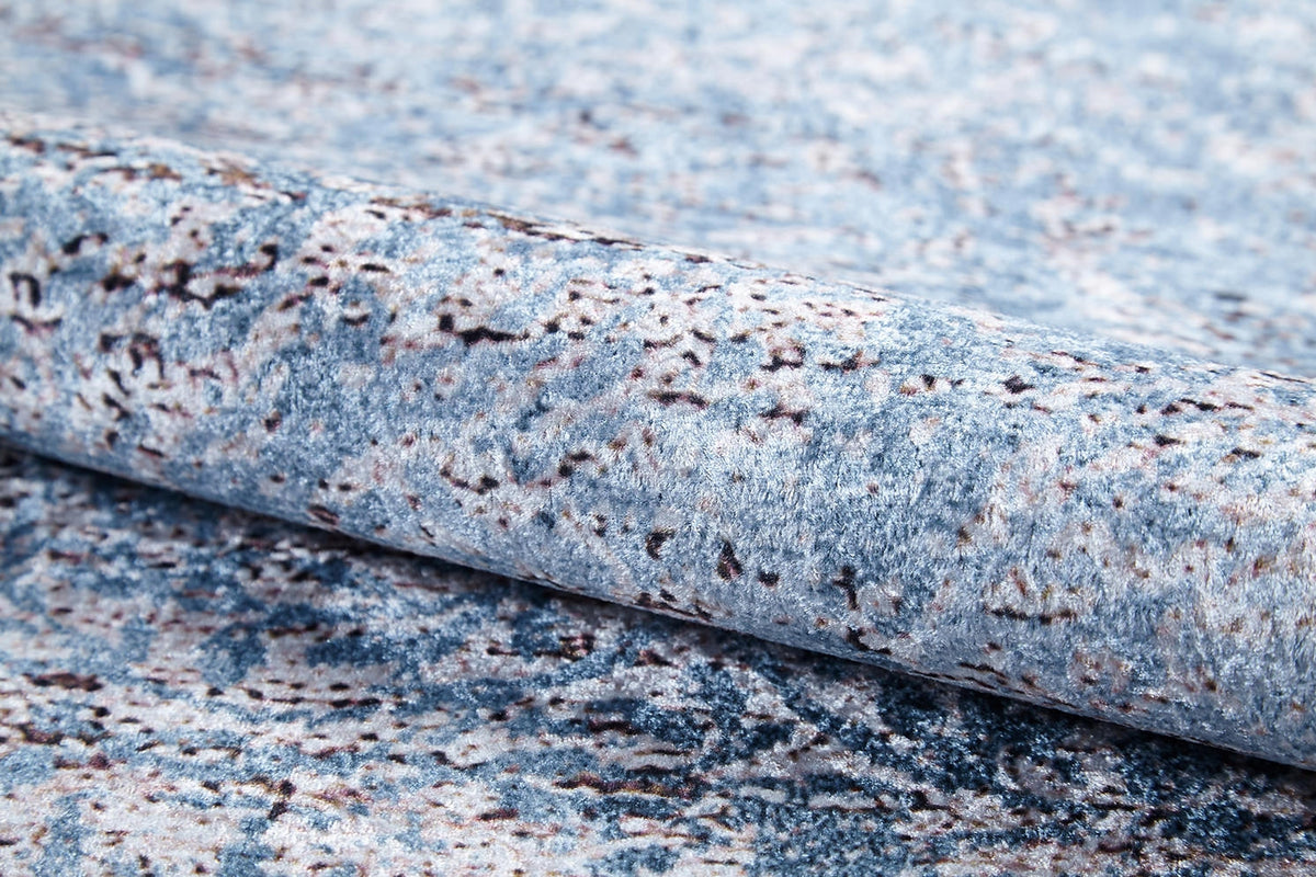 A close-up of the Old World Charm - Washable Rug - JR1606, rolled up to show its blue and gray stone-like abstract texture—ideal for high-traffic areas.