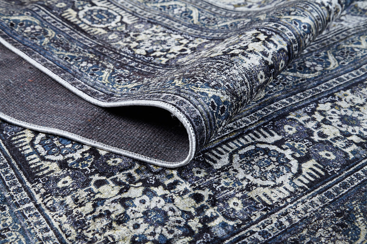A close-up of the Opulent Beauty - Washable Rug - JR1932 in blue, featuring intricate floral and geometric patterns with a folded edge that shows its texture and underside—ideal for high-traffic areas.