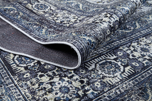 Load image 1 in gallery view. A close-up of the Opulent Beauty - Washable Rug - JR1932 in blue, featuring intricate floral and geometric patterns with a folded edge that shows its texture and underside—ideal for high-traffic areas.