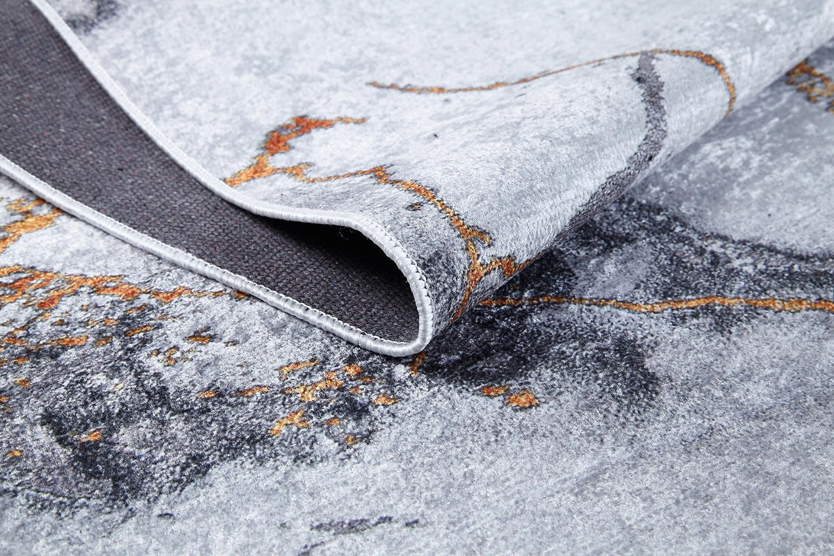 A close-up of the Opulent Veins - Machine-Washable Rug JR1593, featuring a modern abstract gray-anthracite pattern with black and orange accents. One corner is folded to show the underside and stitched edge—ideal for high-traffic spaces.