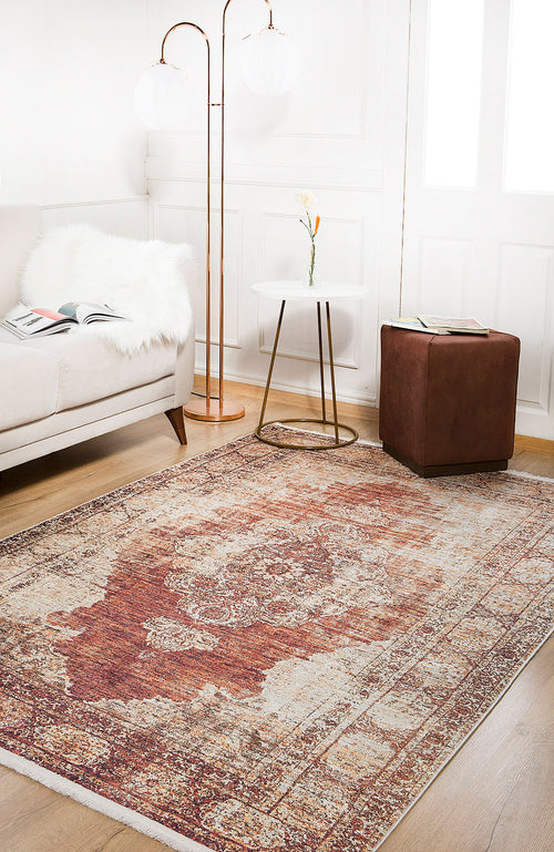 Load image 1 in gallery view. A cozy living room features a beige sofa, brown ottoman, side table with a vase, two tall floor lamps, and the Ornate Grace - Washable Rug - JR1009 in red and beige—perfect for high-traffic areas—on a wooden floor.