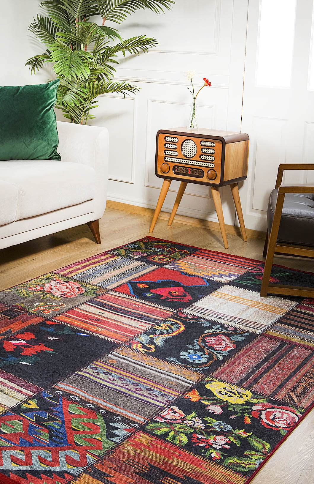 A living room featuring the Petal Paradise - Washable Rug - JR315, a white sofa with green pillow, retro wooden radio on a small table, potted plant, and brown armchair—ideal for high-traffic areas.