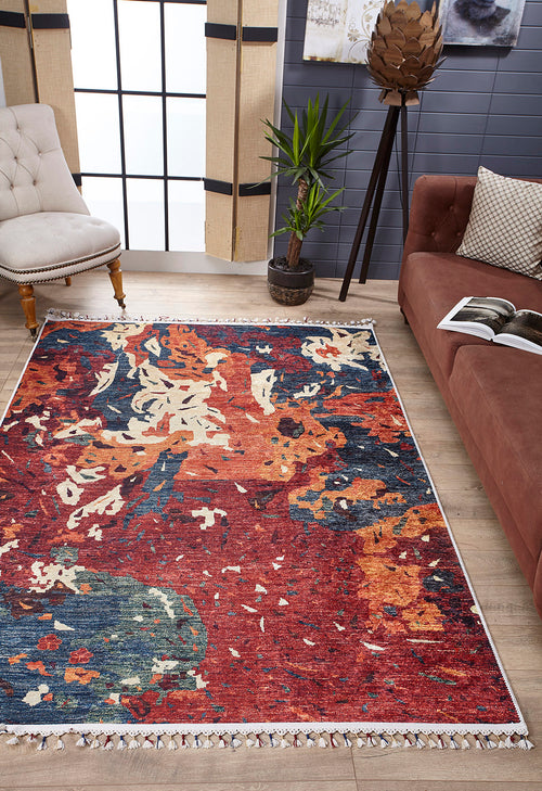 Load image 1 in gallery view. A cozy living room featuring the Psychedelic Splash - Machine-Washable Rug - JR5096, perfect for high-traffic areas, a brown sofa with a patterned cushion, beige tufted chair, potted plant, decorative floor lamp, gray-paneled walls, and large windows.