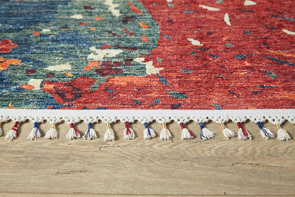 The Psychedelic Splash - Machine-Washable Rug (JR5096), featuring vibrant red, blue, and green patterns with white fringe and colorful tassels, lies on a wooden floor—ideal for high-traffic areas.