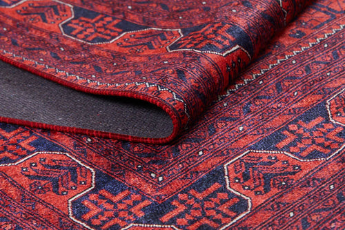 Load image 1 in gallery view. A close-up of the Regal Accents - Washable Rug - JR36 showcases its red and navy geometric pattern, with a corner folded to reveal the underside—ideal for high-traffic areas.