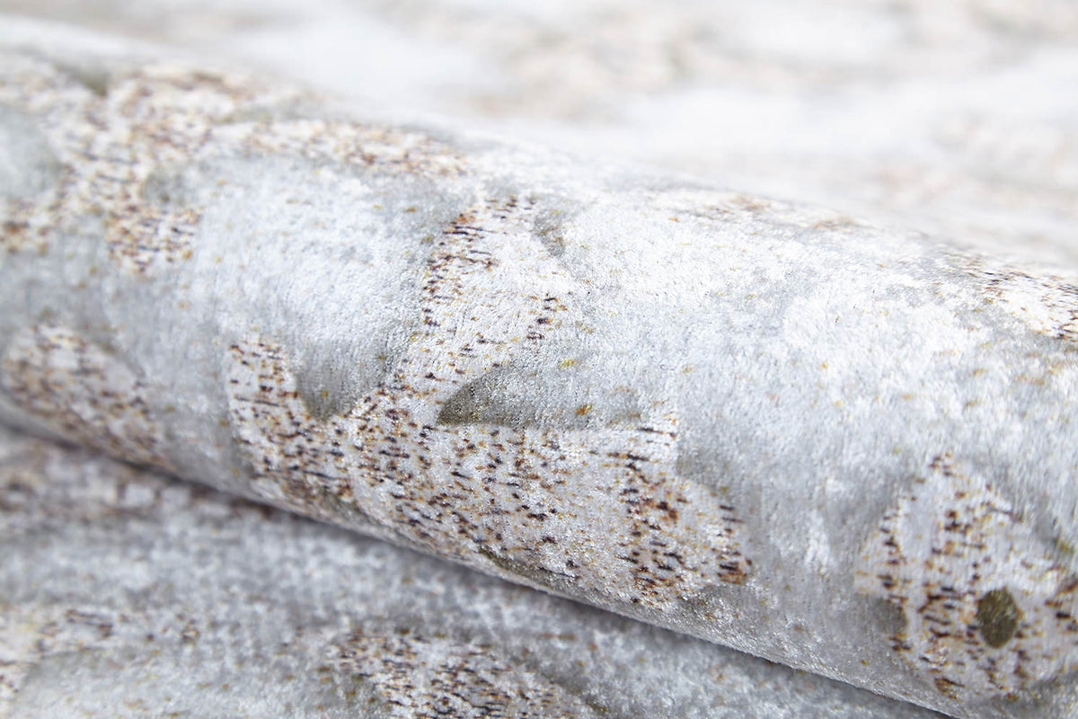 A close-up of the Regal Embellishment - Washable Rug (JR1590) shows a subtle, light gray pattern with brown and beige accents, reminiscent of a gray-anthracite rug. The surface has a slightly metallic or shimmery finish.