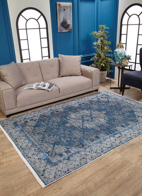 Load image 1 in gallery view. A beige sofa with cushions sits behind an open book, next to the Regal Insignia - Washable Rug - JR1786 on wooden flooring. Blue paneled walls, arched windows, a potted plant, and side tables complete this modern living room for high-traffic areas.