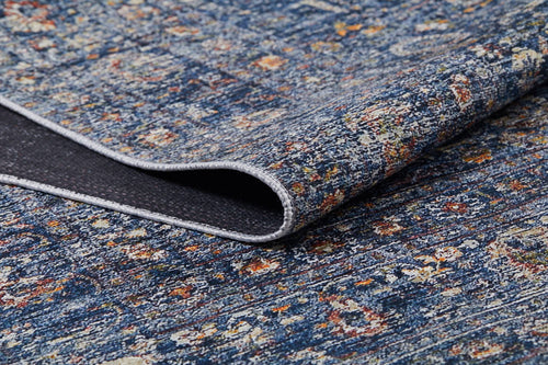 Load image 1 in gallery view. A close-up of the Regal Splendor - Washable Rug - JR1017 shows its blue, multicolored abstract pattern with yellow, orange, and white accents. A folded corner reveals the dark non-slip backing on this textured rug, ideal for high-traffic areas.