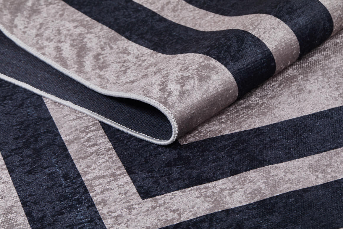 Close-up of the Regal Trellis - Washable Rug - JR601, showing its geometric pattern with wide textured light gray and dark navy stripes. This allergy-friendly rug is partially folded to display its thickness and texture.