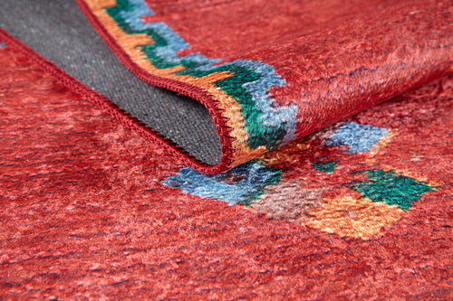 Load image 1 in gallery view. A close-up of the Rosy Blush - Machine-Washable Rug (JRS5067) shows its red, textured surface with colorful geometric patterns and a folded corner revealing a dark gray underside—durable and perfect for high-traffic areas.