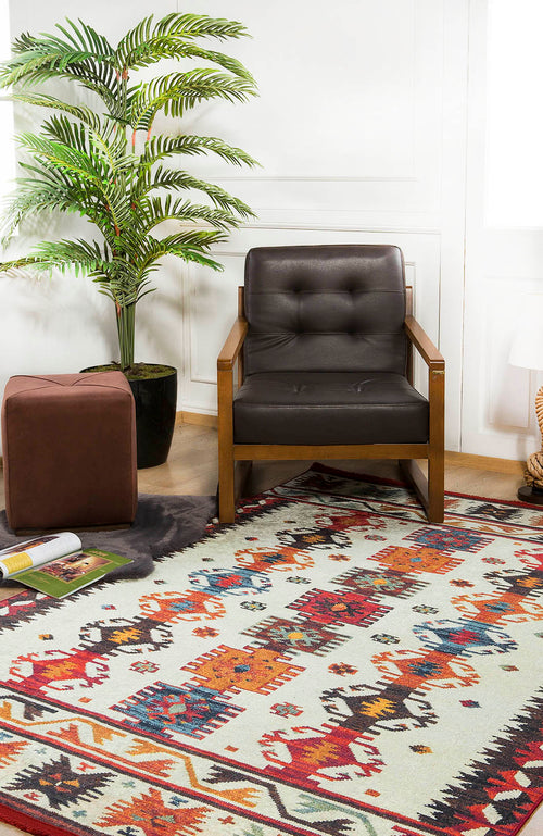 Load image 1 in gallery view. A cozy room corner with a brown armchair, a Rustic Refrain - Washable Rug - JR149 featuring geometric designs, a brown ottoman, a potted plant, and magazines on the floor near a white wall.