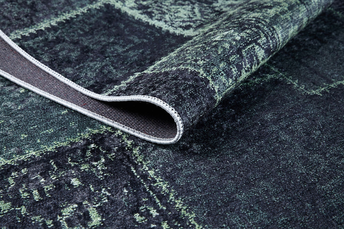 A close-up of the Rustic Remix - Washable Rug - JR1710 in green and black, featuring a folded corner that displays its stitched edge and underside—durable and washable, ideal for high-traffic areas.