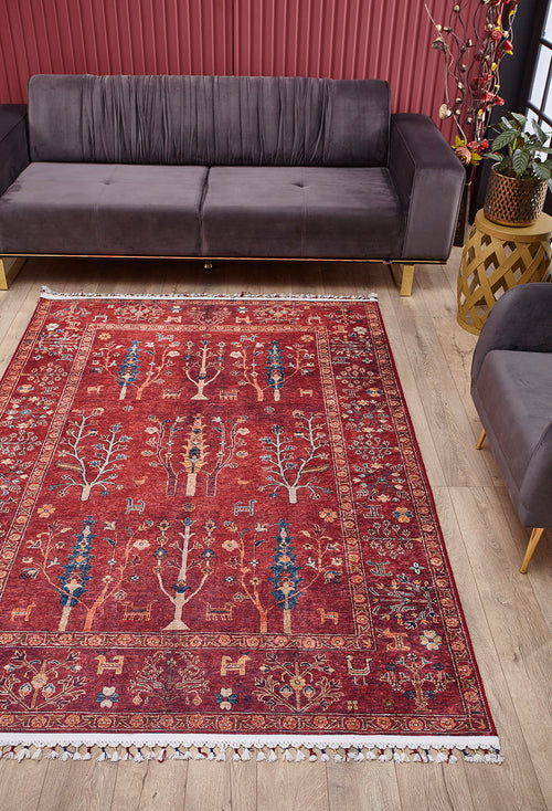 Load image 1 in gallery view. The Rustic Retreat - Washable Rug - JR5095 in vibrant red, featuring tree and animal motifs, sits on a light wood floor between a gray sofa and armchair—perfect for high-traffic spaces with stylish red wall panels behind.