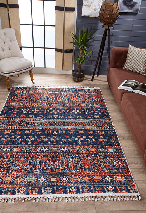 Bild 1 in Galerieansicht laden. A living room featuring the Sahara Sunrise - Washable Rug - JR5091, ideal for high-traffic areas, a brown couch with an open book, a beige tufted chair, a potted plant, and large windows letting in natural light.